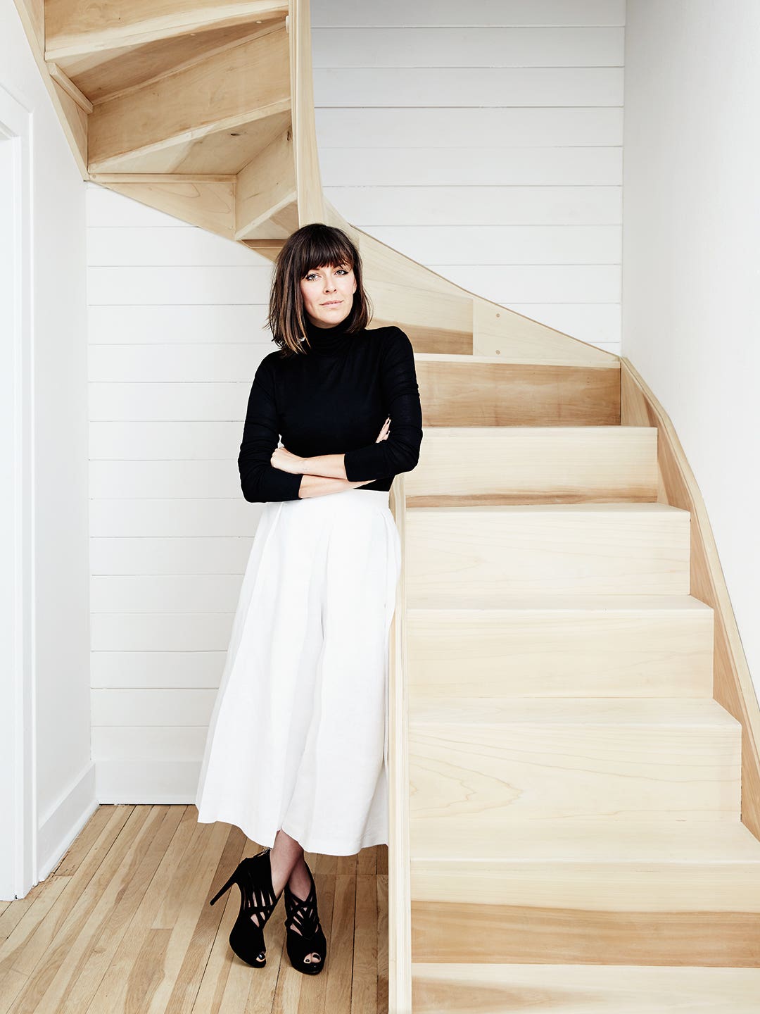 Woman standing by staircase wearing white pants and a black turtleneck