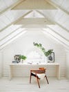 Desk space in a white a-frame room with wooden chair
