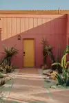 Pink house exterior with yellow door flanked by palm trees.