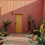 Pink house exterior with yellow door flanked by palm trees.