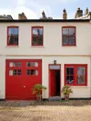 Traditional cream-colored London mews home exterior with bright red door and window trim.