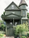 Victorian house exterior painted completely in forest green with steps down to sidewalk.