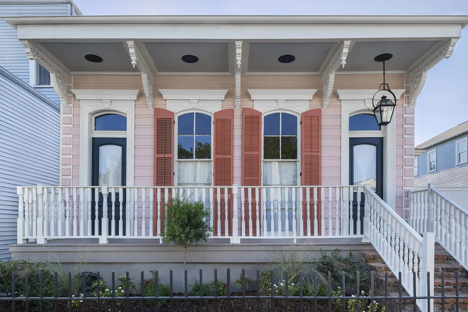 New Orleans-style house exterior painted light pink with darker pink shutters and white balcony.