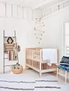 White nursery with textiles hanging on ladder and wooden mobile. 
