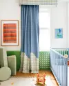 Nursery with blue curtain, red graphic art, and green cushions. 