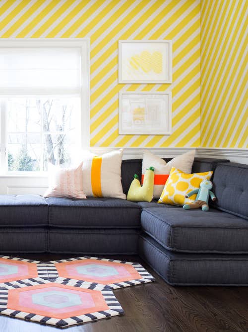 sectional couch in front of yellow and white striped wallpapered wall