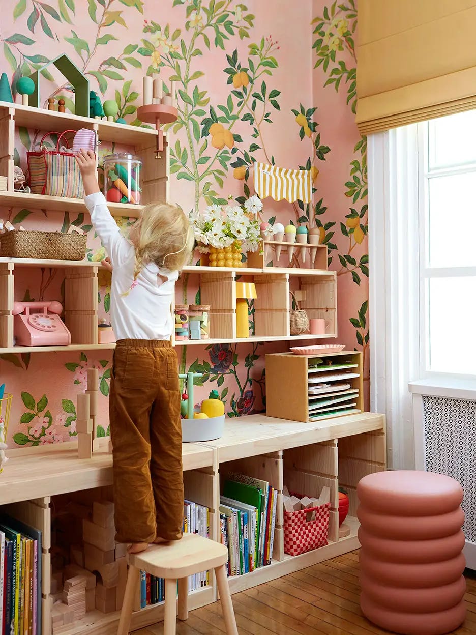 Little girl reaching up to reach toy shelf in her pink floral bedroom.