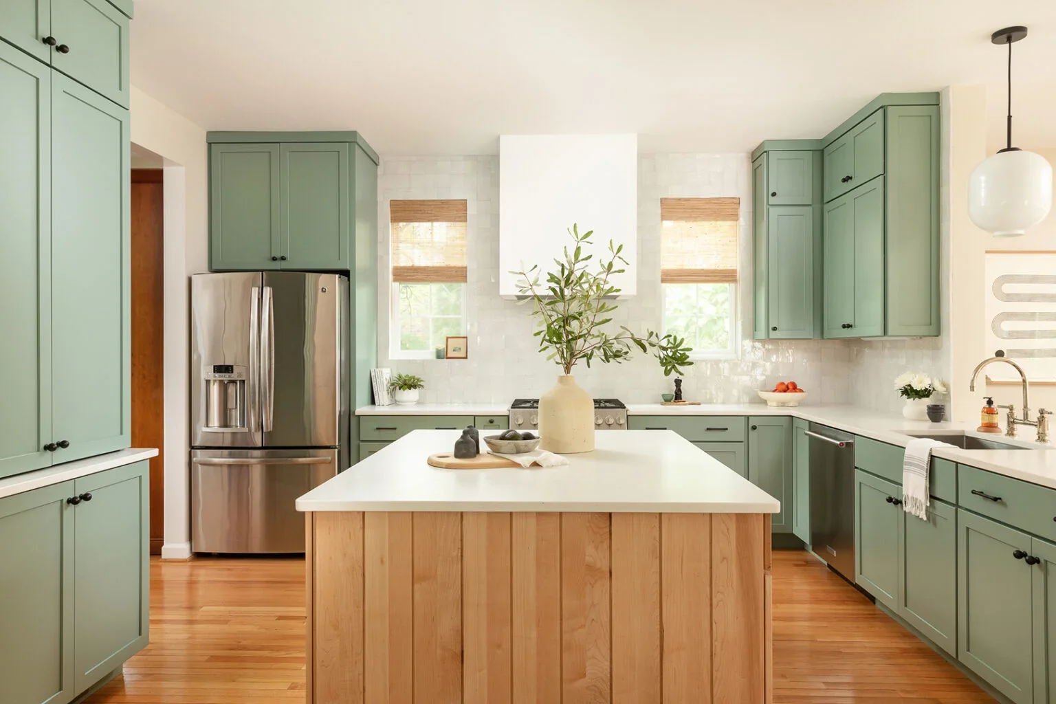 Sage green kitchen cabinets with wood island.