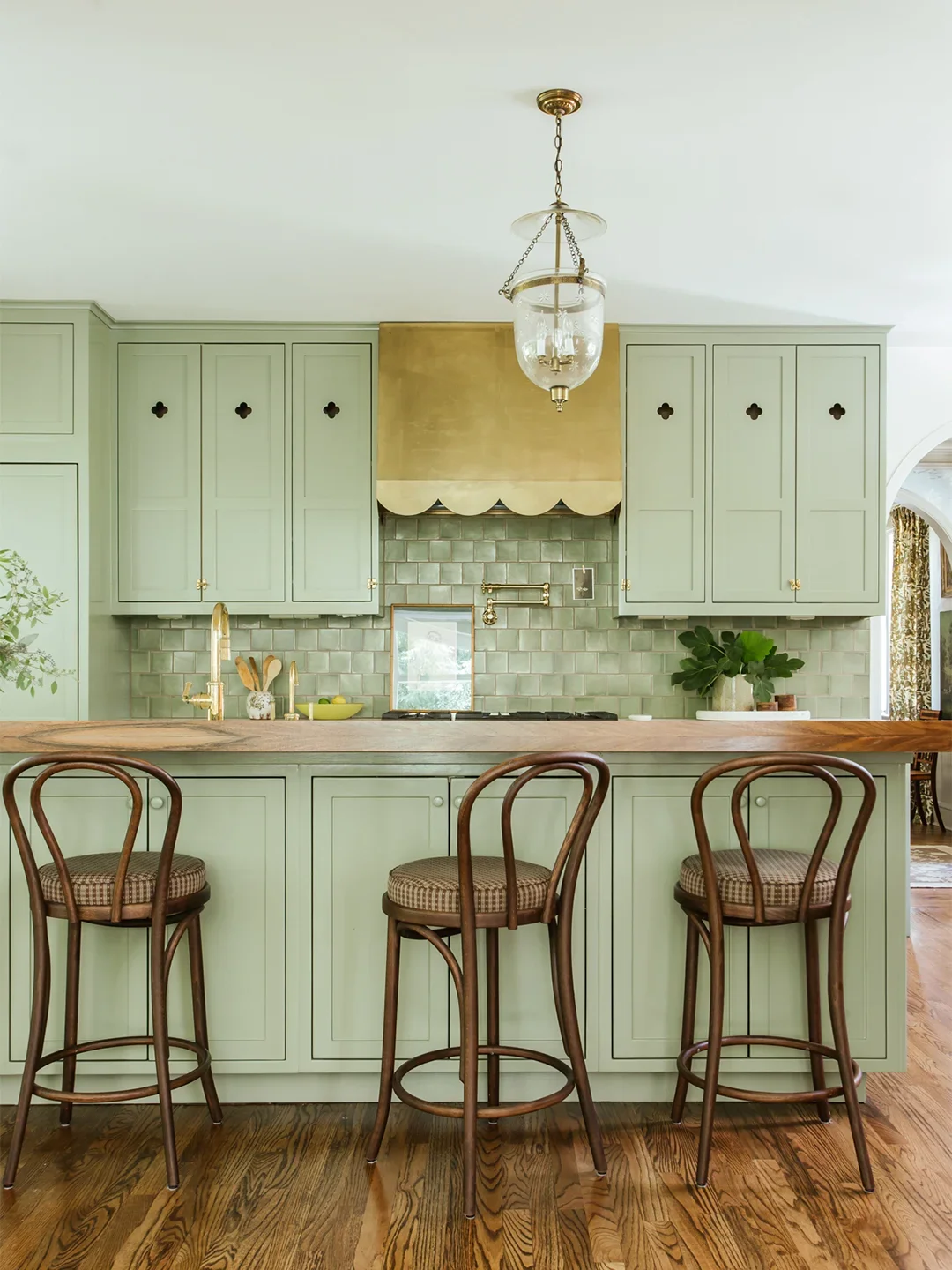 Sage green kitchen cabinets with brass scalloped hood. 