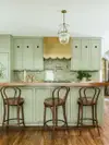 Sage green kitchen cabinets with brass scalloped hood. 