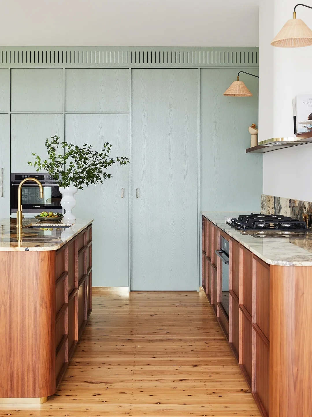 Kitchen with wood cabinets and island, and sage green cupboards along back wall. 
