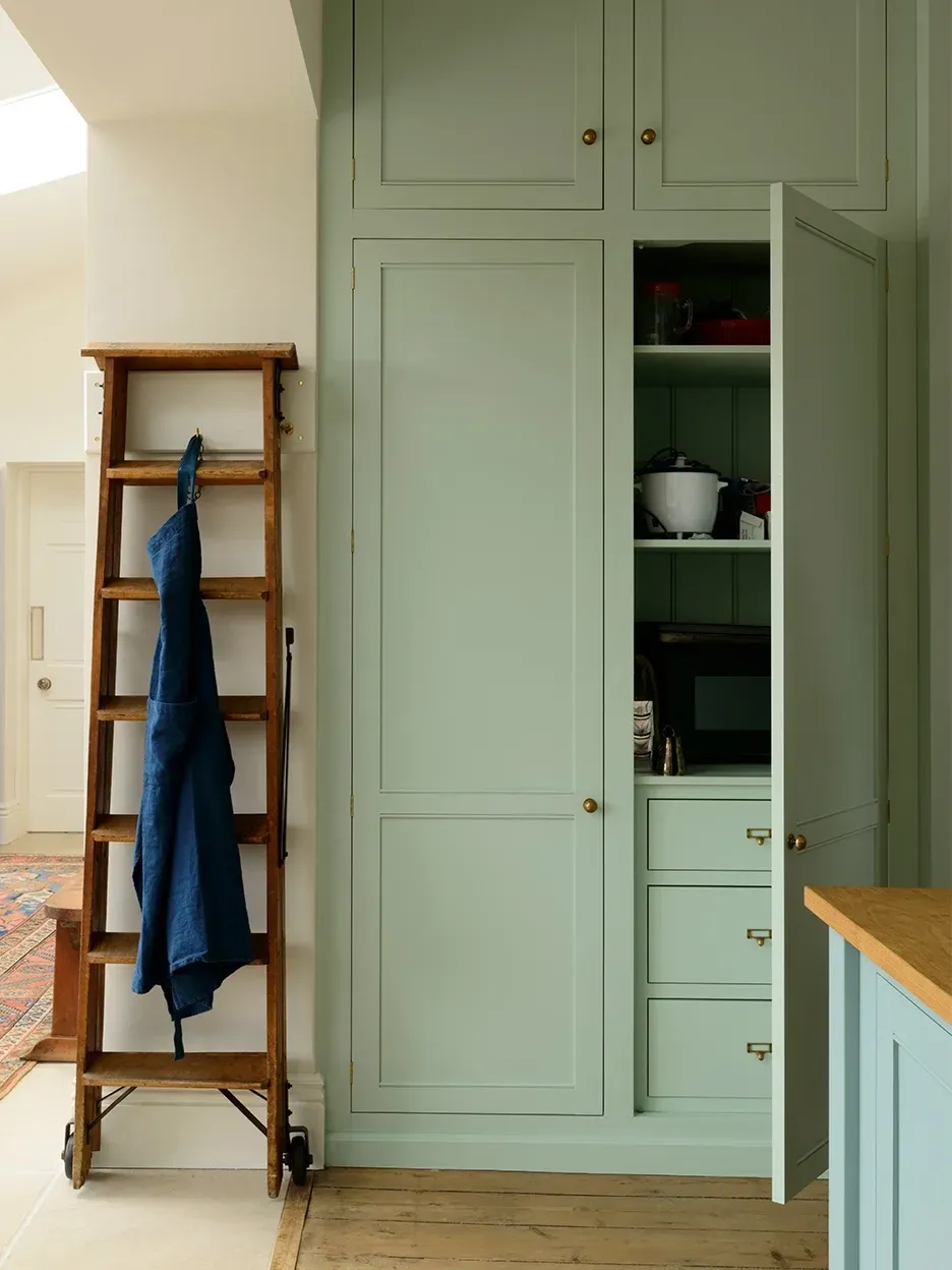 Wood ladder leaning on sage green kitchen cabinet doors.