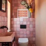 Pink-tiled small bathroom with pink sink and artwork that says "Discotheque."