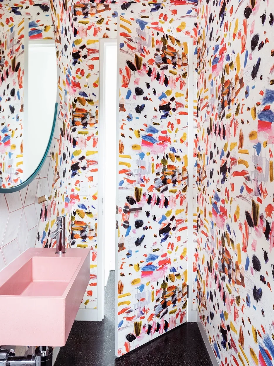 Small bathroom with paint stroke-like wallpaper and pink sink.