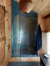 Small bathroom with wood walls and steel-lined shower. 