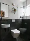 Tiled small bathroom with shower with white tiles on top and black tiles on bottom. 