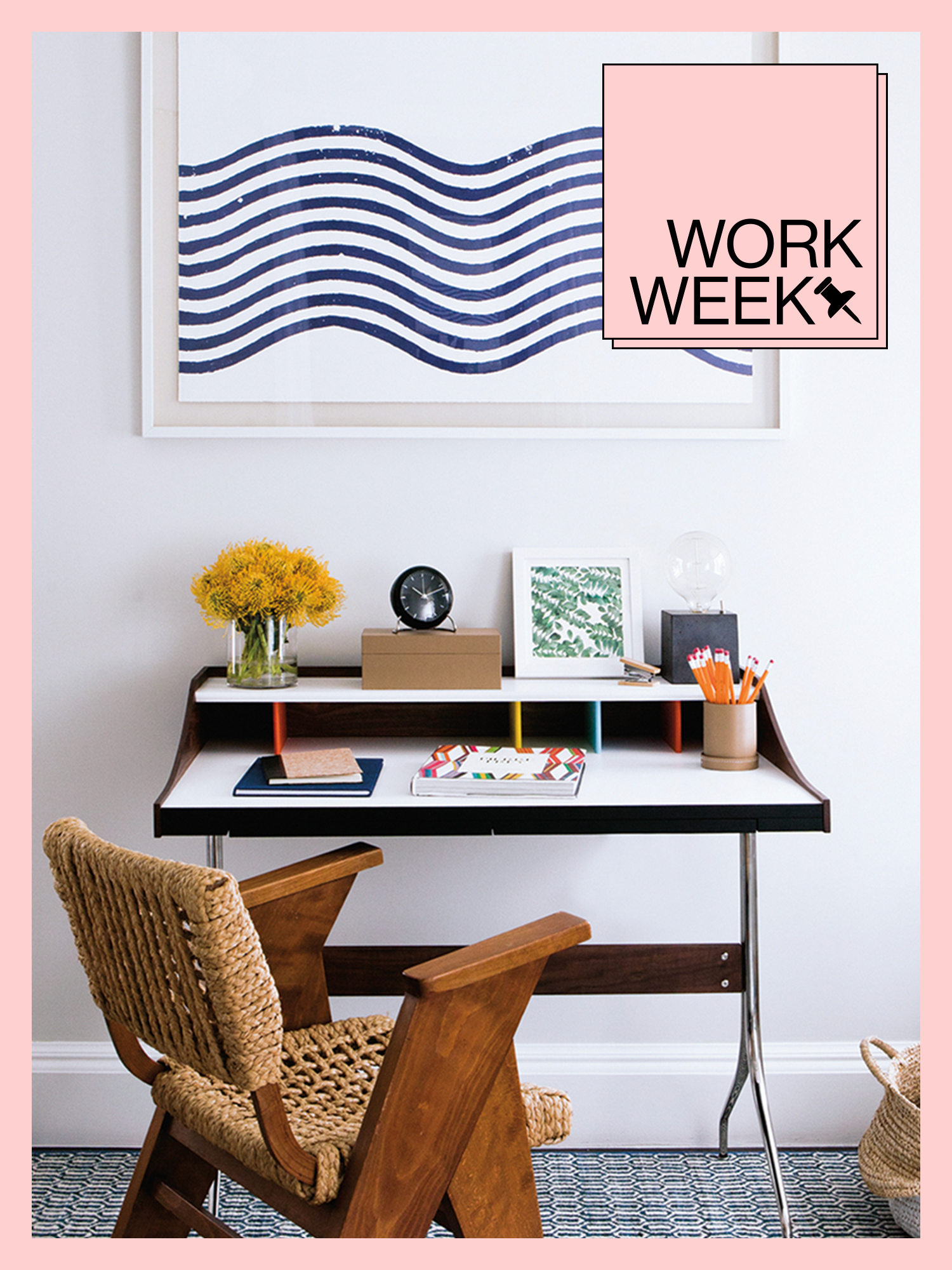 Small-space desk with blue wavy artwork above it and a woven wooden chair beside it.