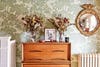 Dresser topped with dried florals in front of green wallpapered wall