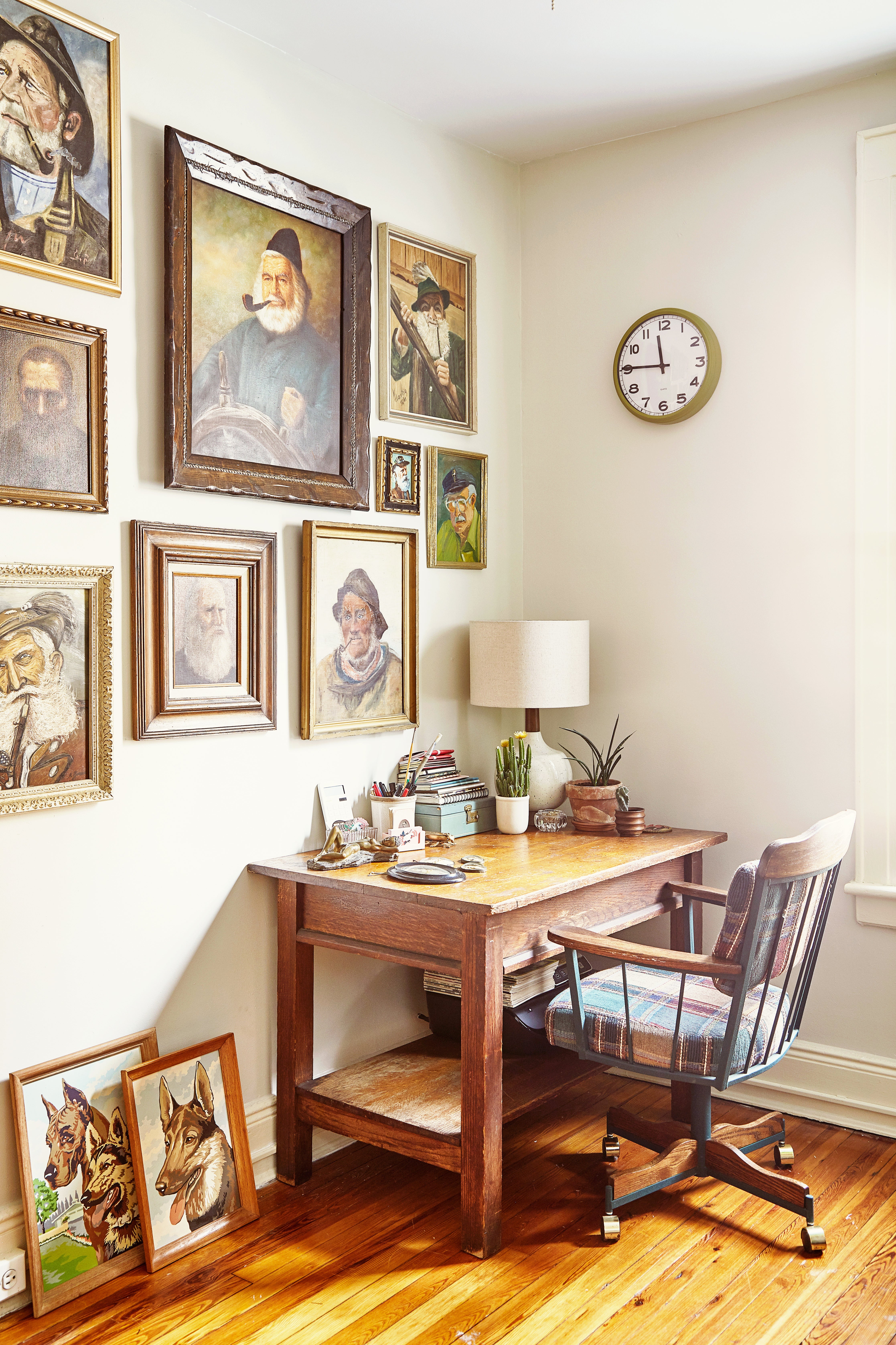 Office with framed old-fashioned paintings on gallery wall; wooden desk with chair