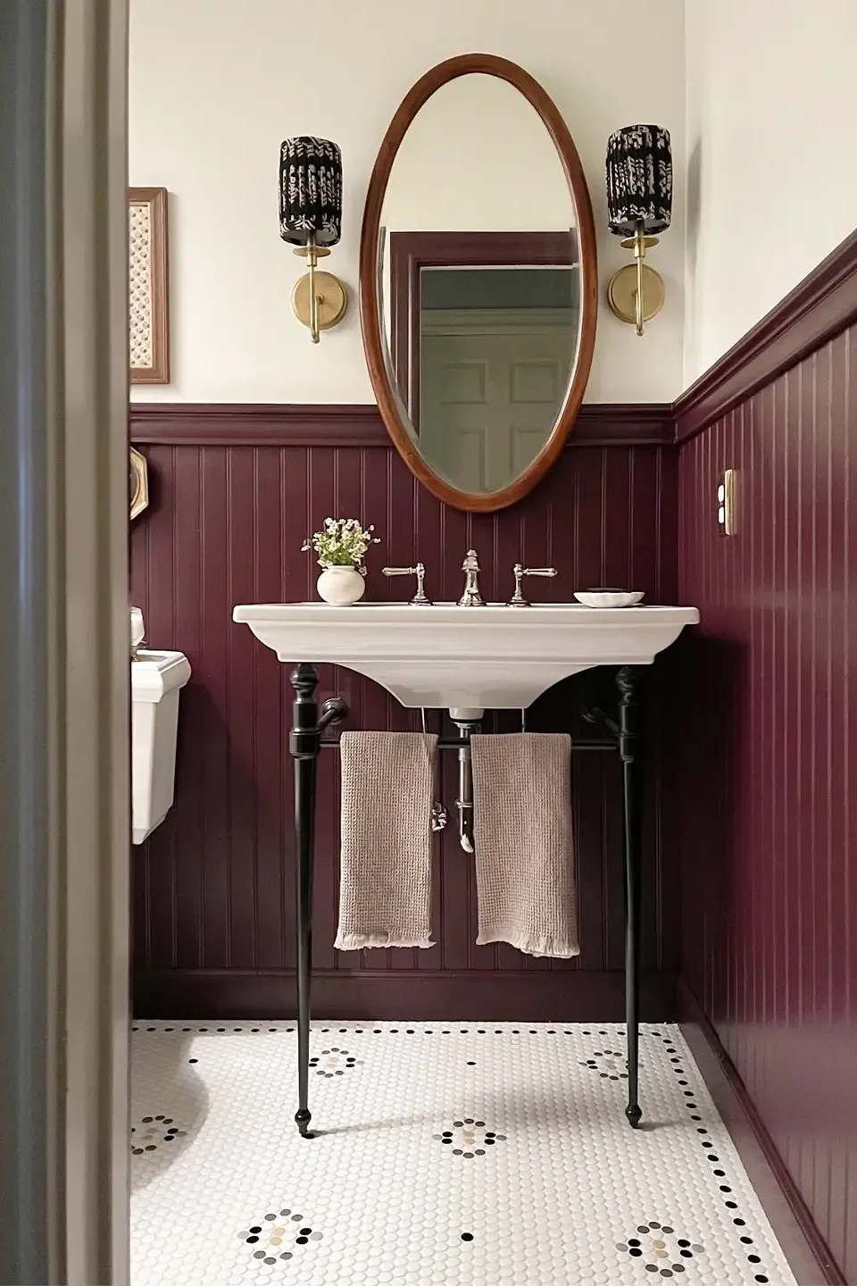 Bathroom with burgundy wainscoting and oval mirror.