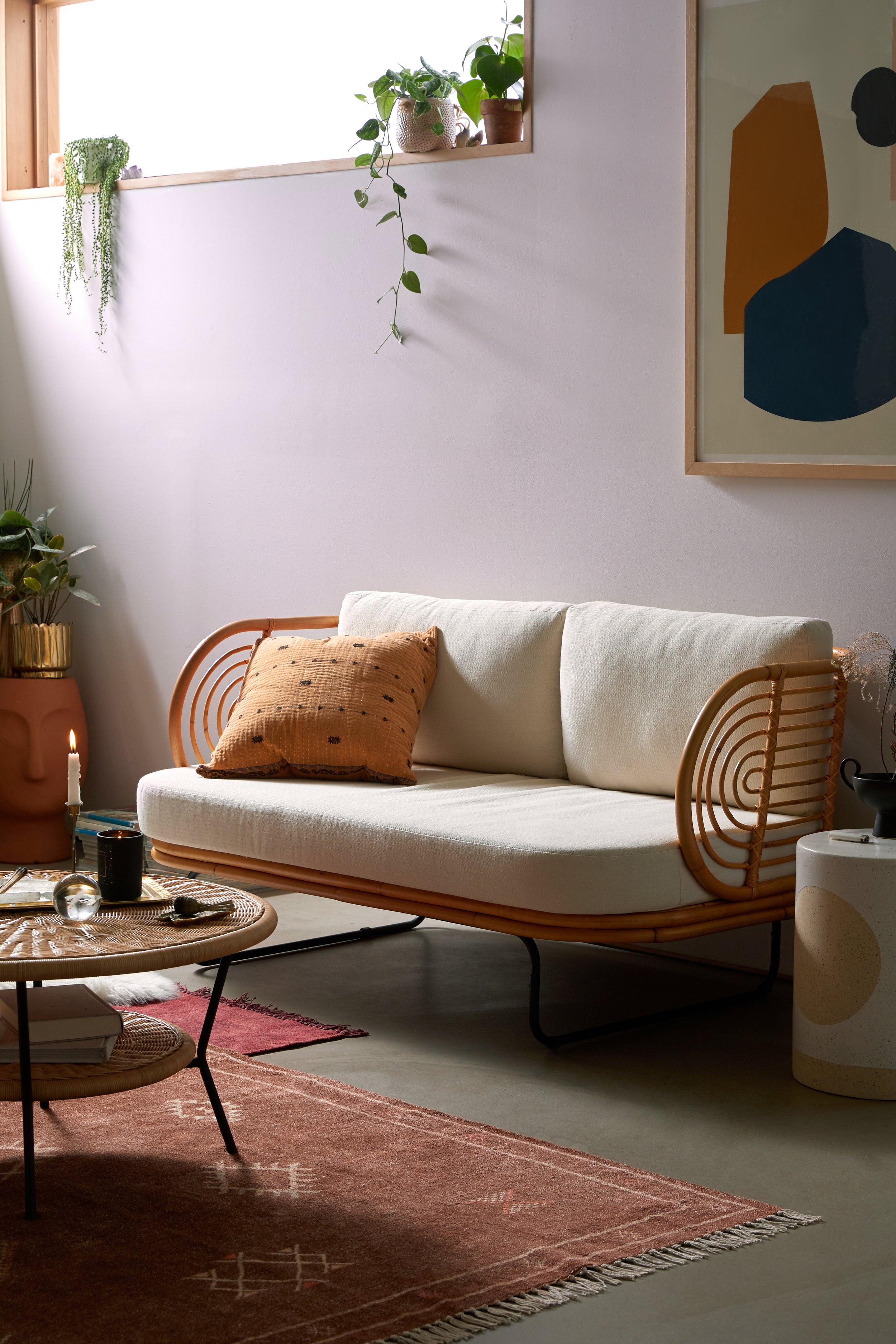 Living room with light purple walls, bohemian rattan sofa with white cushions and rattan coffee table