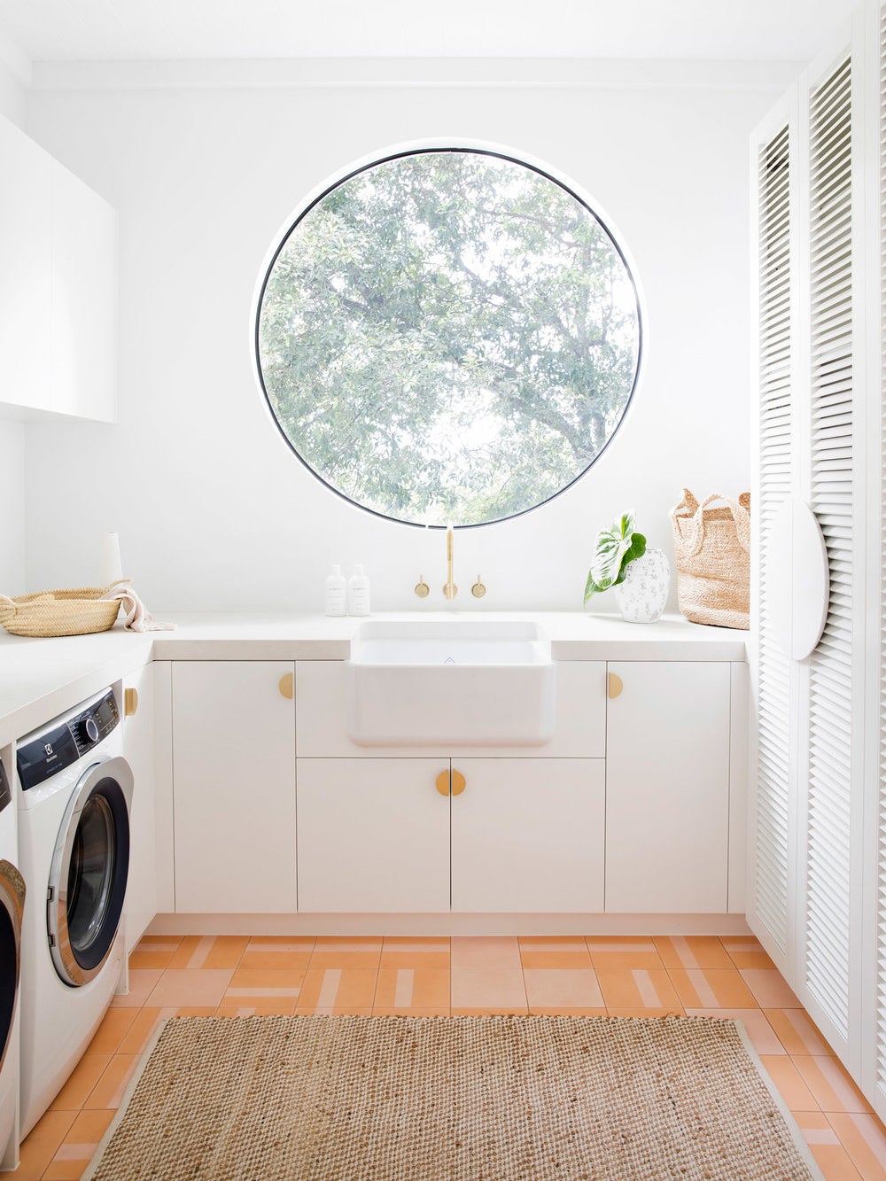 round window in a white laundry room with orange and pink tiles