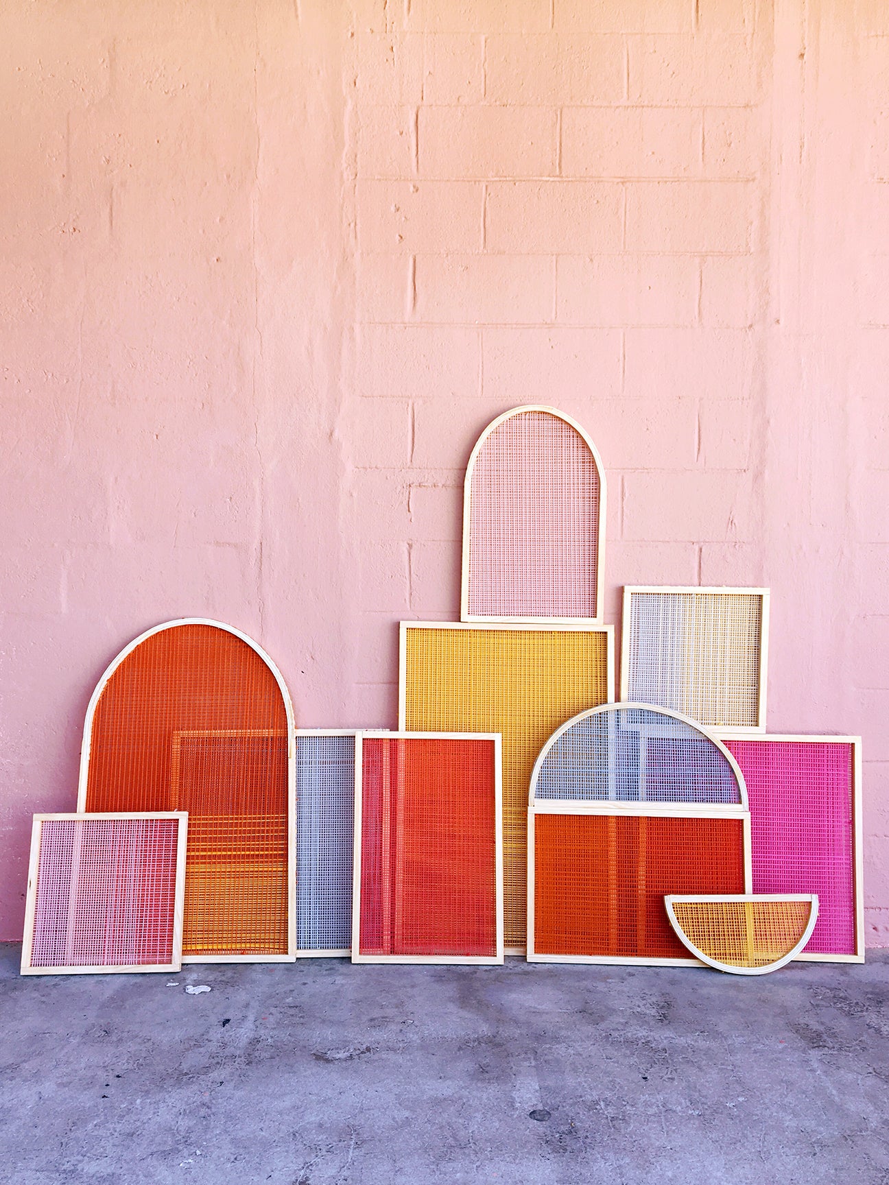 colorful woven wall hangings leaning against a pink exterior wall
