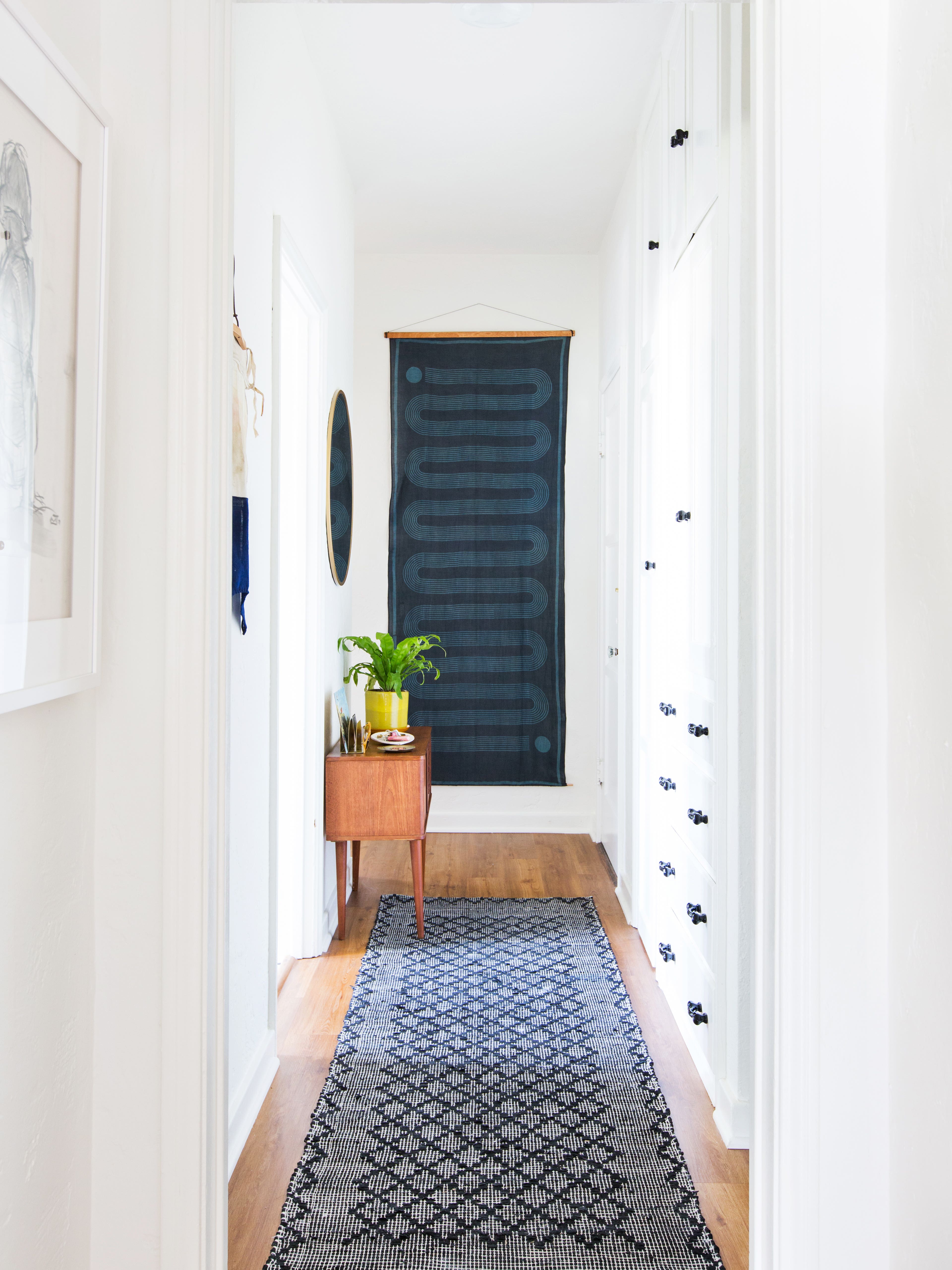 white hallway with a blue runner and blue wall hanging at the end