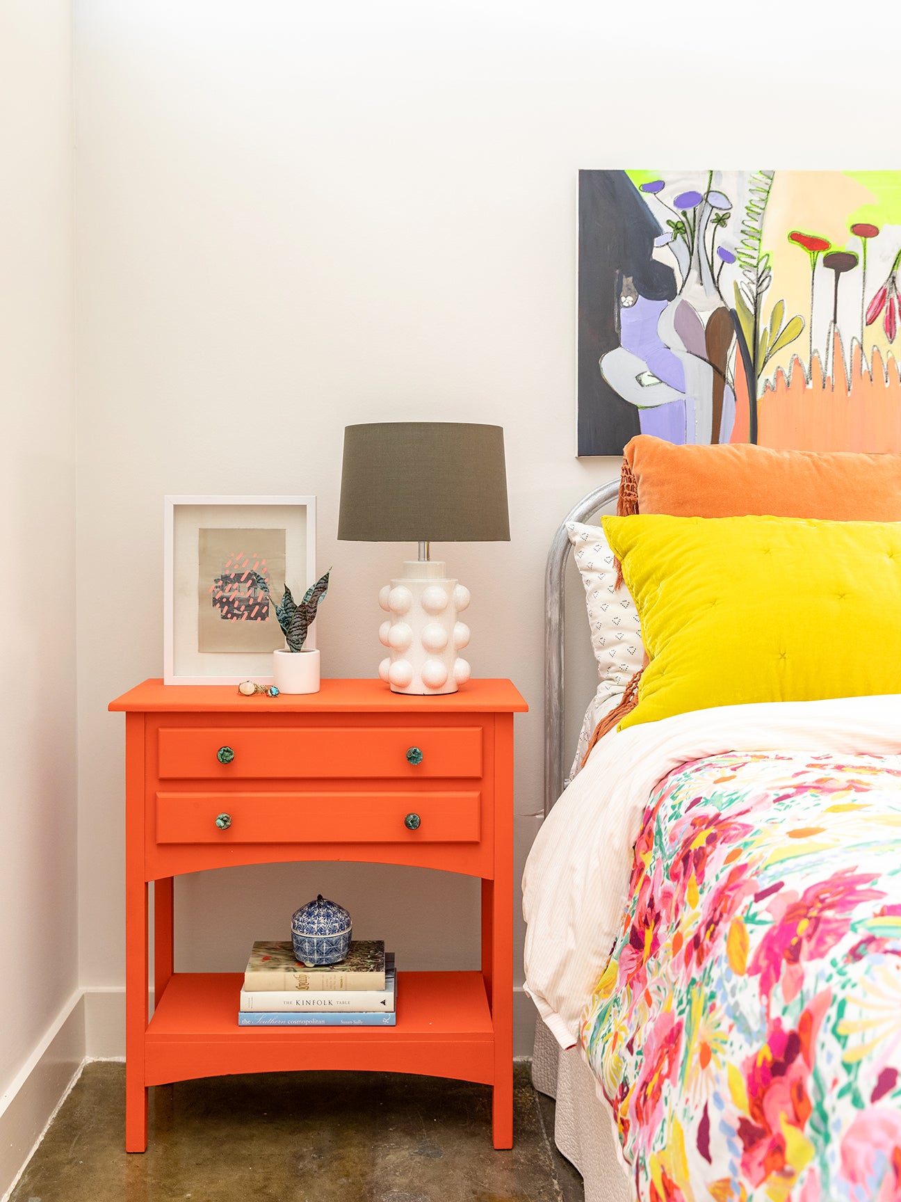 bright orange nightstand next to a floral bed