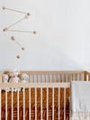 wood mobile hanging over a crib with terracotta colored sheets