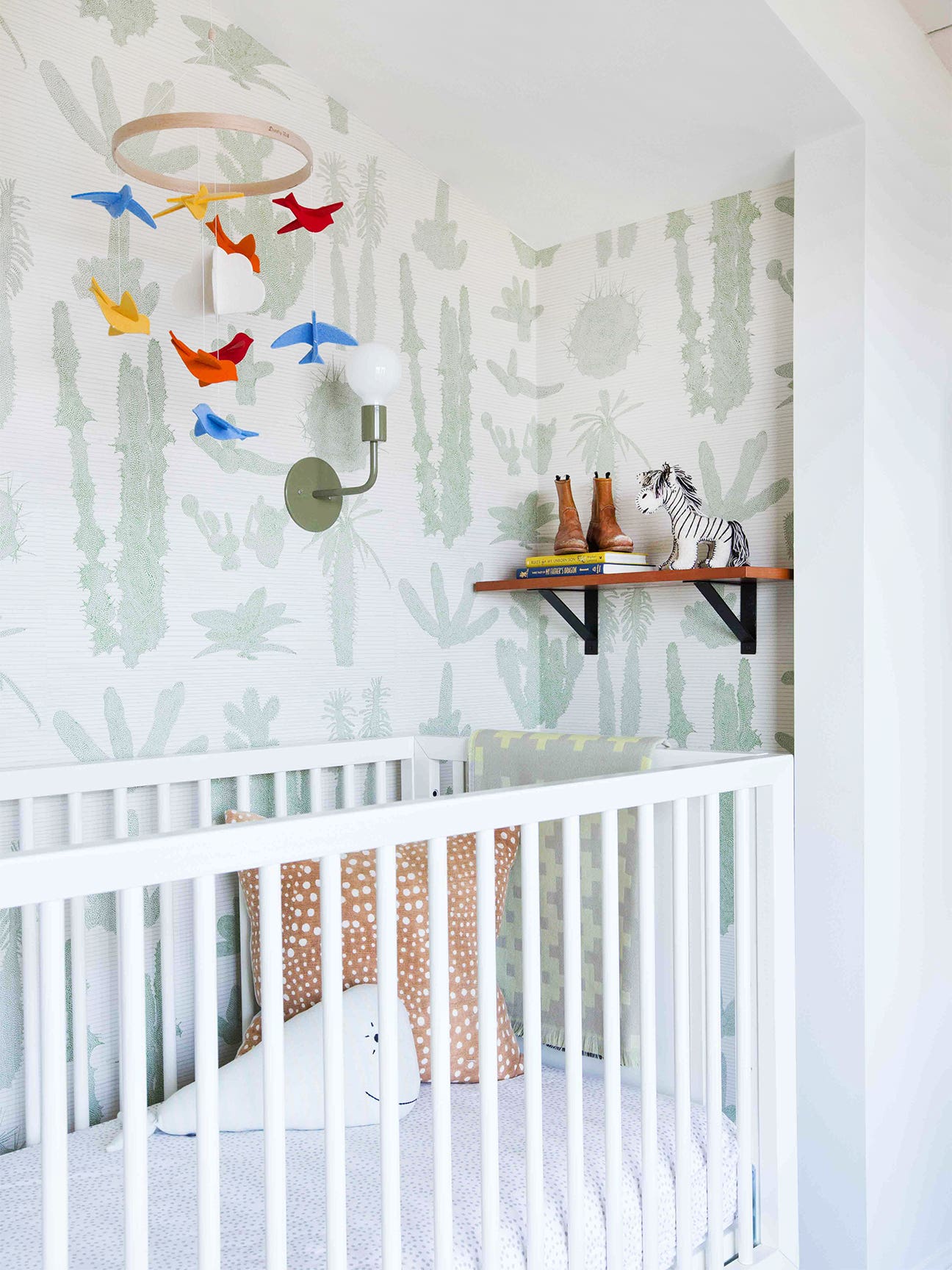 wallpapered nursery with a crib and a colorful mobile