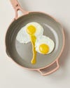 A pink skillet with two eggs cooking on the surface