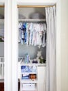 small closet with baby clothes and a curtian drawn back