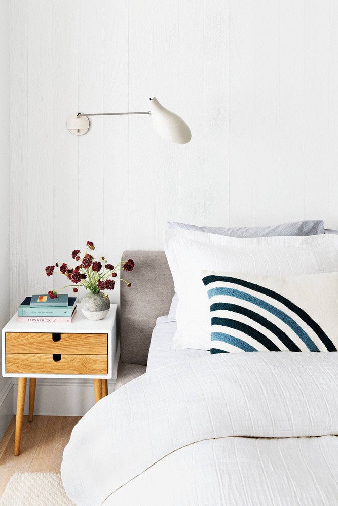 White bedroom with blue striped pillow and wooden nightstand