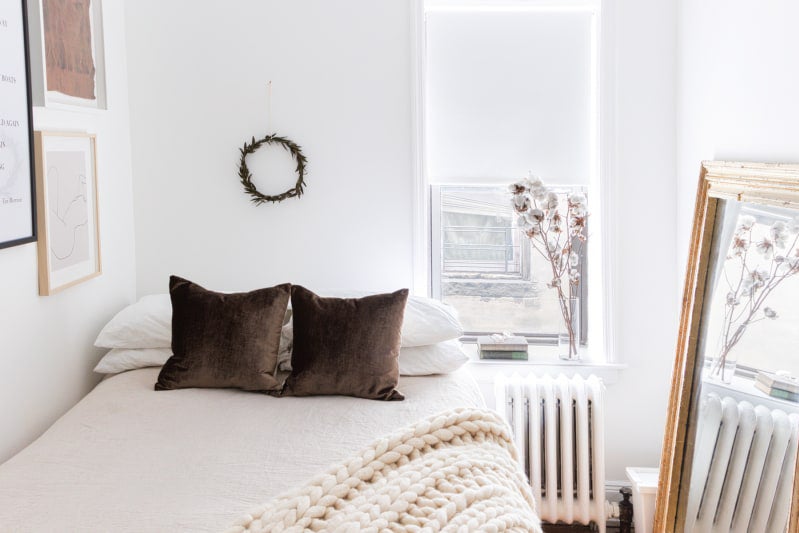 white bedroom with brown velvet pillows and wreath above bed