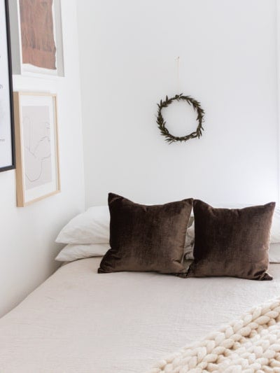 white bedroom with brown velvet pillows and wreath above bed