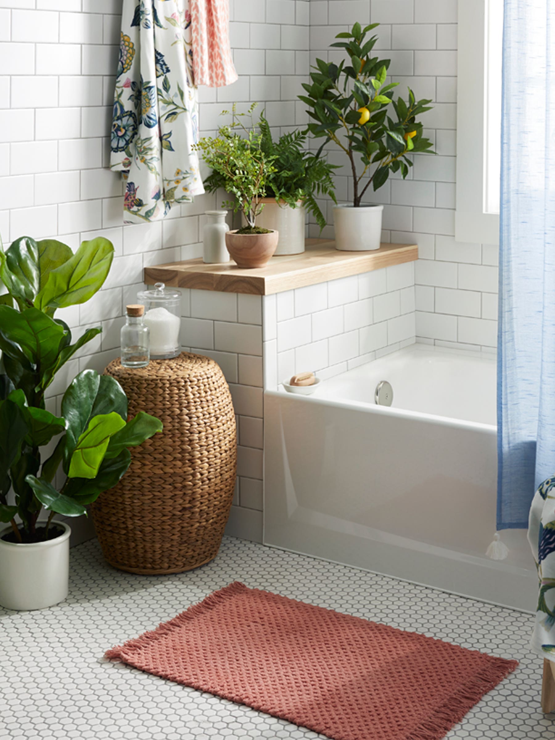 white bathroom with blue shower curtain, plants, and pink bathmat