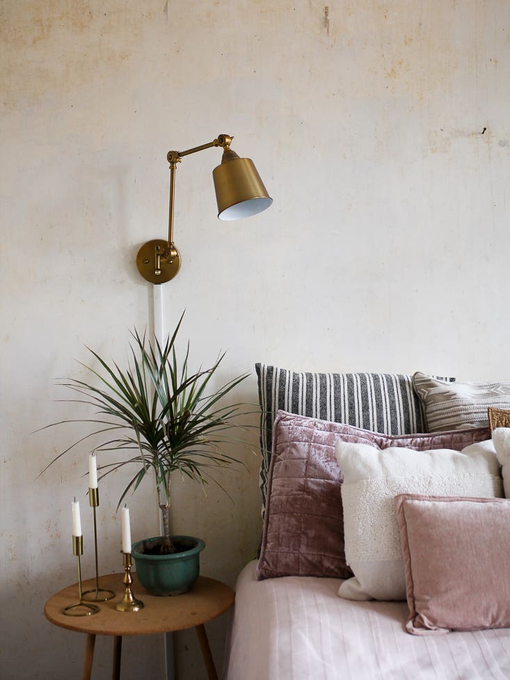 bed with muted pink pillows and brass sconce