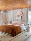 pink and orange bed with modern wood ceiling and gray drapes