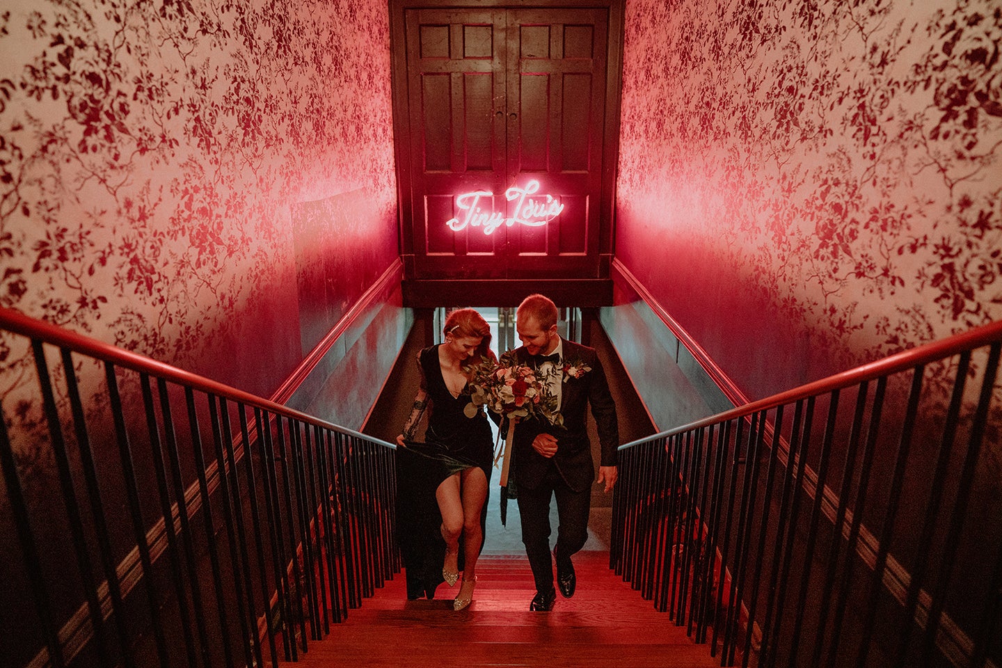 couple walking up stairs with pink neon sign