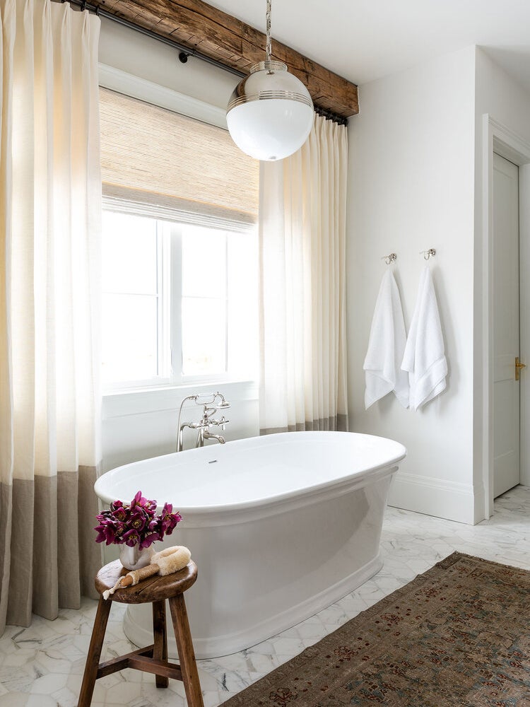 bathtub in front of curtains and rustic wood beam