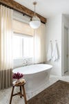 bathtub in front of curtains and rustic wood beam