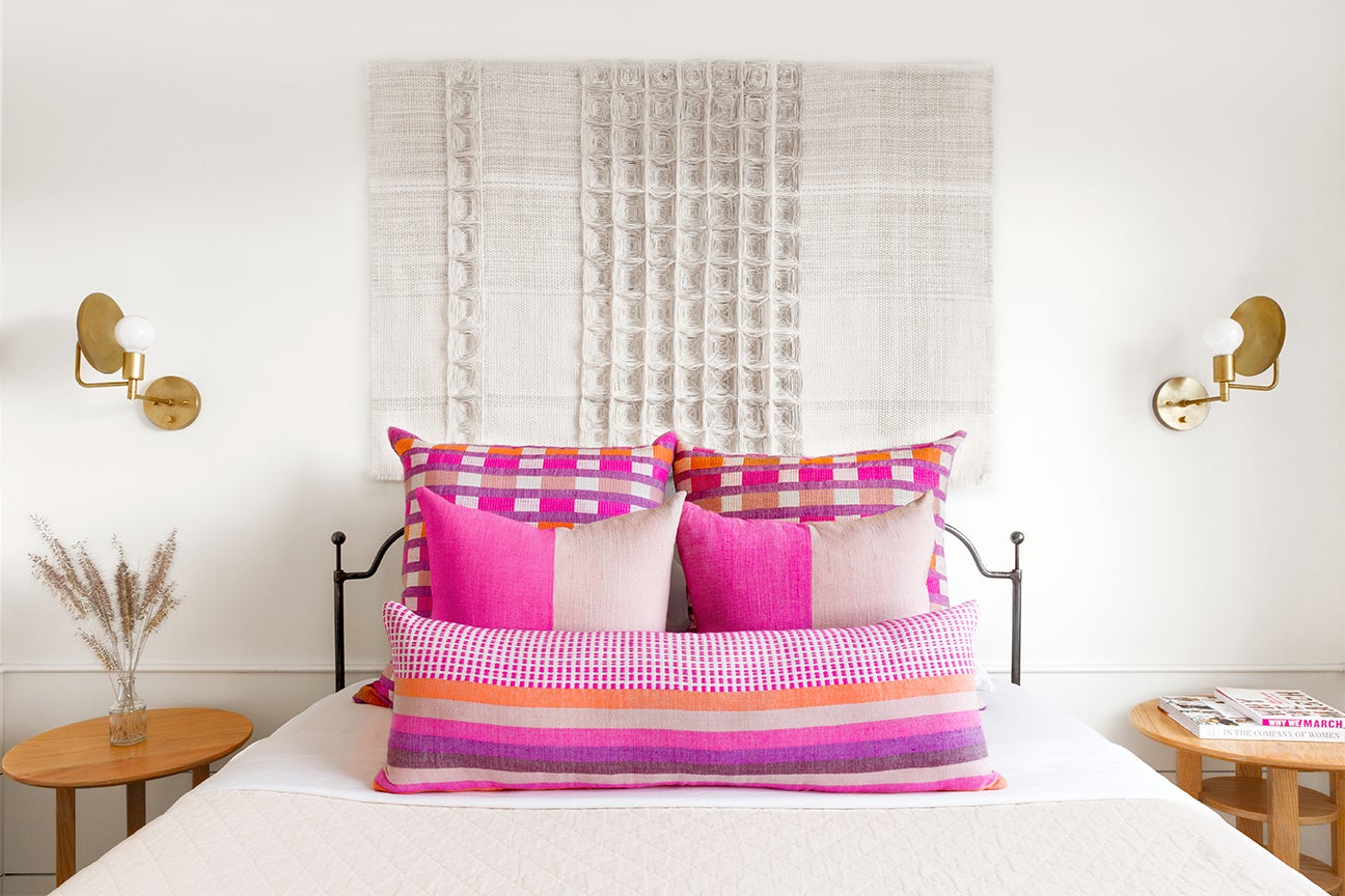 white bed with bright pink pillows and a hanging tapestry behind it