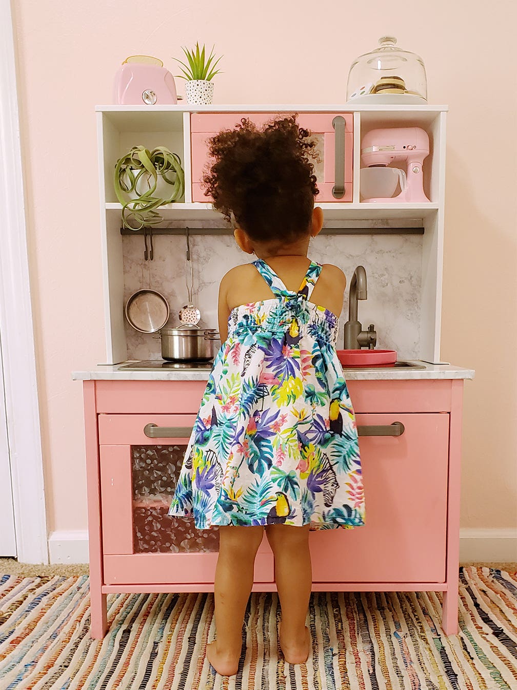 Toddler in front of pink play kitchen