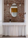 brick wall with oval mirror and sink skirt