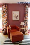 pink room with orange-printed curtains and orange armchair
