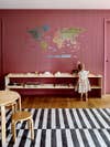 Little girl faces mauve wall with wood shelves and world map decal.