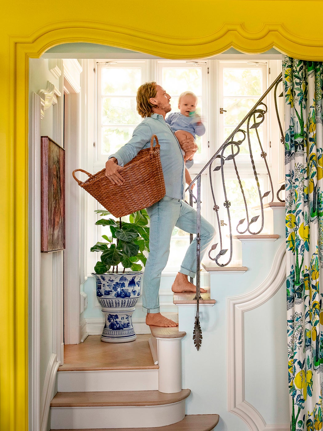 Man on stairs holding baby and laundry basket.