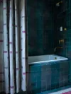 Deep teal tiled bathtub with purple and grey shower curtain.
