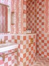 Coral bathroom with checkerboard tile and squiggly-lined wallpaper.